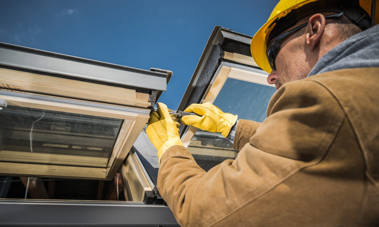 Caucasian Worker Wearing Safety Helmet and Protective Gloves Carrying Out Repair Works on Roof Skylight Windows Using His Screwdriver.